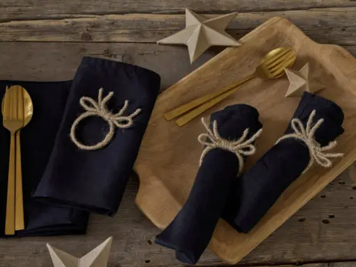 Serviettenringe selber machen: Dunkle Stoffservietten mit rustikalen Geweih-Motiven aus Jute, dazu goldene Besteckteile und Papiersterne.