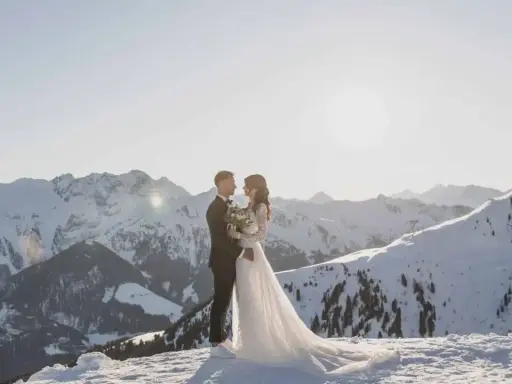 Ein Brautpaar steht sich in der verschneiten Berglandschaft gegenüber. Ihre **Hochzeit im Schnee** ist ein magischer Moment vor der Kulisse schneebedeckter Gipfel.