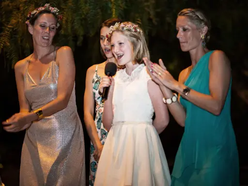 Mädchen hält Mikrofon, während ihre Schwester und andere Frauen bei einer Hochzeitsrede applaudieren.