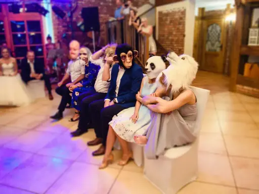 Gäste in Tiermasken warten auf kurzweilige Hochzeitsspiele. Ein Affe, ein Panda und ein weißes Tier sind zu sehen.