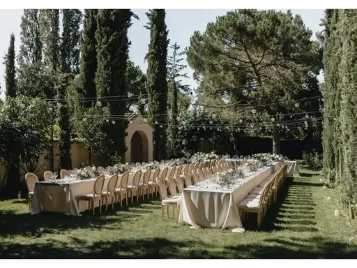 Festlich gedeckte lange Tafel im Garten, umgeben von Zypressen und Bäumen. Perfekt für Hochzeitslocation-Fragen.