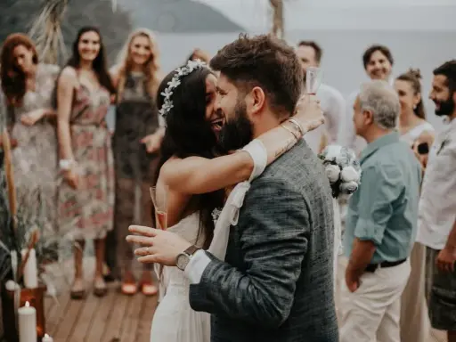 Glückliches Brautpaar umarmt sich, Gäste im Hintergrund. Perfekt für zitate hochzeitskarte.