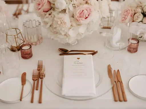 Ein festlich gedeckter Tisch mit Blumen, Gläsern und roségoldenem Besteck. Ein Hochzeitsmenü für Susan, perfekt arrangiert vom wedding planer.