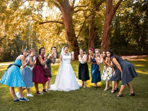Brautjungfern in Polka-Dot-Kleidern und die Braut in Weiß posieren für eine fröhliche Rockabilly-Hochzeit im Freien.