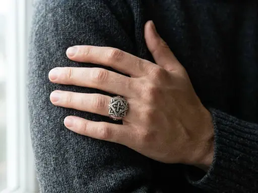 Ein Mann trägt einen detailreichen Ring mit Kreuzmuster an der linken Hand.