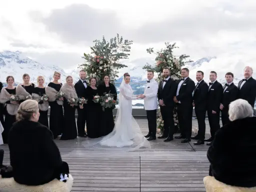 Brautpaar und Hochzeitsgesellschaft vor schneebedeckten Bergen. Eine wunderschöne Hochzeit in den Bergen mit Brautjungfern in schwarzen Kleidern und Männern in Anzügen.