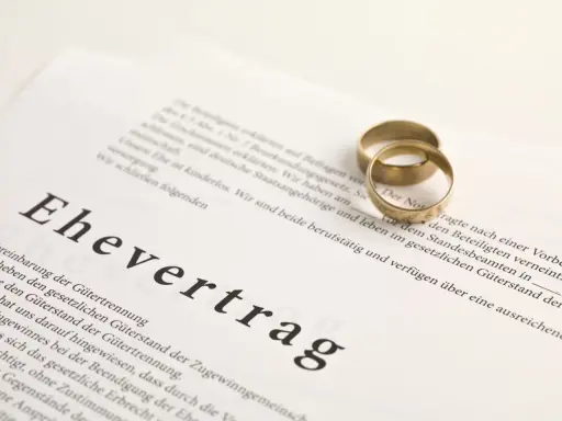 Zwei goldene Eheringe liegen auf einem Dokument mit der Überschrift "Ehevertrag". Eine Ehevertrag Vorlage, die die rechtlichen Vereinbarungen für die Ehe festhält.