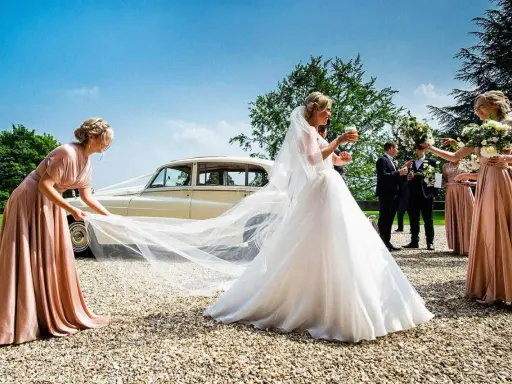 Brautjungfern helfen der Braut mit ihrem Schleier vor einer Hochzeitslimousine.