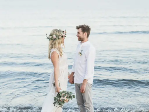 Ein glückliches Paar feiert seine Hochzeit am Strand zu zweit. Die Braut trägt einen Blumenkranz, der Bräutigam ein weißes Hemd.