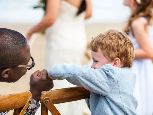 Ein Mann mit Brille hält die Hand eines Jungen. Im Hintergrund heiratet mein Sohn.