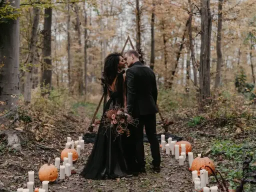 Ein Brautpaar küsst sich im Wald bei Kerzenlicht und Kürbissen. Eine romantische Halloween-Hochzeit im Herbst.