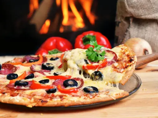Eine dampfende Pizza mit Salami, Oliven und Paprika, perfekt für den Mitternachtssnack zur Hochzeit, vor einem knisternden Kaminfeuer.
