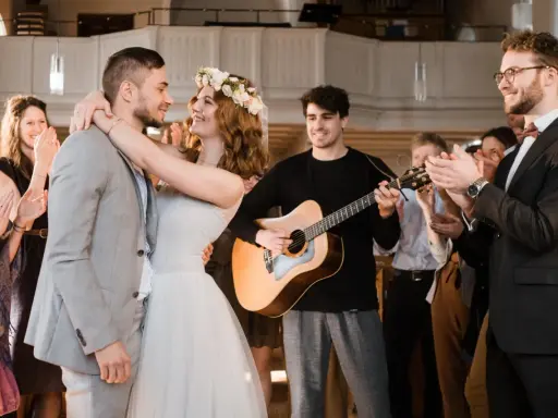 Glückliches Brautpaar umarmt sich, während ein Gitarrist spielt und Gäste applaudieren. Die Stimmung ist festlich, wie bei schönen Hochzeitsliedern auf Deutsch.