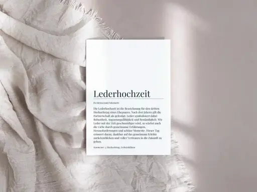 Ein Blatt Papier mit dem Text "Lederhochzeit" und einer Erklärung liegt auf einem hellen Stoff. Der Text beschreibt die Bedeutung der ledernen Hochzeit als Symbol für eine gefestigte Partnerschaft.