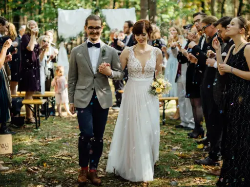 Brautpaar schreitet durch Seifenblasen, Gäste feiern Hochzeit locker.