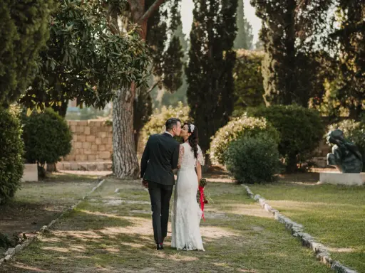 Ein Brautpaar küsst sich im Park. Die Braut trägt ein Spitzenkleid, der Bräutigam einen dunklen Anzug. Eine kroatische Hochzeit im Grünen.
