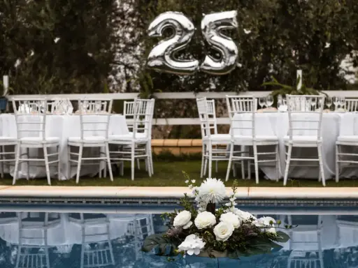 Festlich gedeckte Tische mit weißen Stühlen und Luftballons "25" über ihnen – perfekt für eine Rede zur Silberhochzeit am Pool.