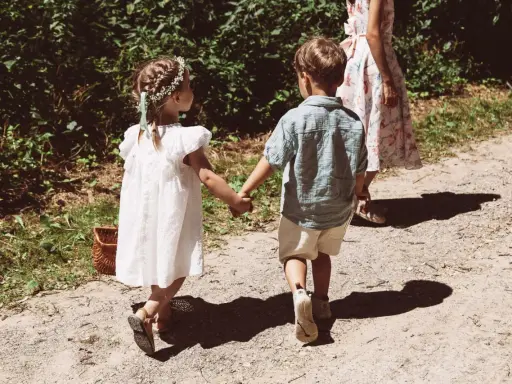 Zwei Kinder, ein Mädchen mit Blumenkranz und ein Junge, halten Händchen auf dem Weg zu einer Hochzeit mit Kindern.