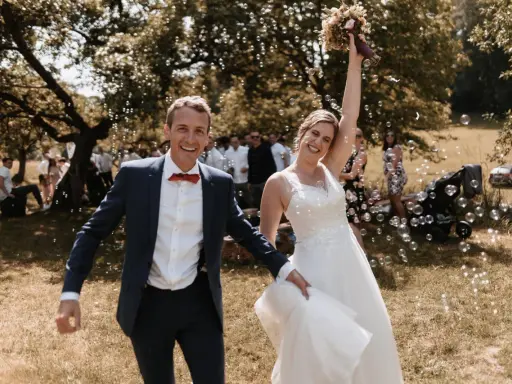 Glückliches Brautpaar im Freien, umgeben von Seifenblasen. Sie strahlen und scheinen gerade ihren Hochzeitstanz gelernt zu haben und feiern diesen besonderen Moment.