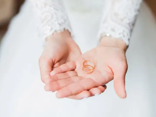 Zwei goldene Eheringe liegen in den Händen einer Braut. Sie sind ein Symbol für ihre bevorstehenden Hochzeitstage und die Namen, die sie für immer verbinden werden.