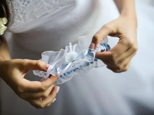 Braut hält ein weißes Strumpfband mit blauen Akzenten. Das Strumpfband ist ein traditionelles Symbol für Glück bei der Hochzeit.