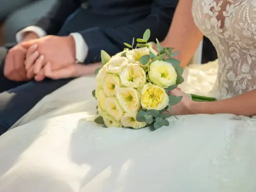 Brautpaar hält Händchen, Brautstrauß mit gelben Rosen. Eine Hochzeit Versicherung gibt Sicherheit für den großen Tag.