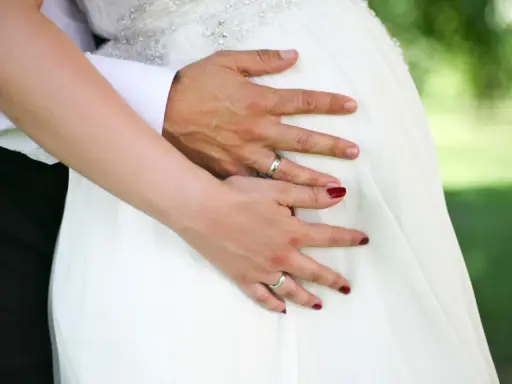 Hände auf dem Bauch einer schwangeren Braut im weißen Kleid. Ein Paar heiratet voller Vorfreude.