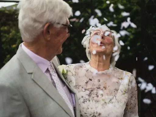 Ein glückliches Paar, meine Eltern, feiern diamantene Hochzeit. Konfetti fliegt durch die Luft, während sie sich anlächeln.