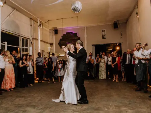 Brautpaar tanzt langsamer Walzer zu deutschen Liedern, während Gäste zusehen und fotografieren.