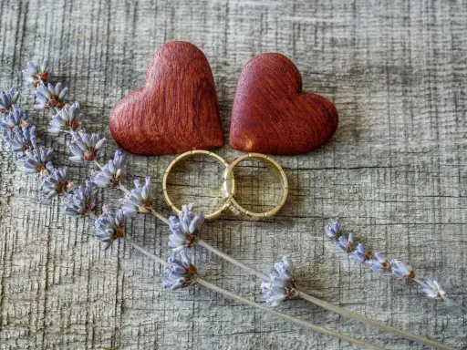 Zwei Holzherzen, Eheringe und Lavendelzweige auf Holz. Ein schöner Anblick für einen 5. Hochzeitstag Spruch.