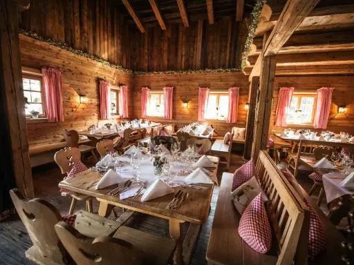 Gemütliche Holzhütte, festlich gedeckte Tische für eine Egerner Alm Hochzeit. Rote Karovorhänge und Blumen schmücken den rustikalen Raum.
