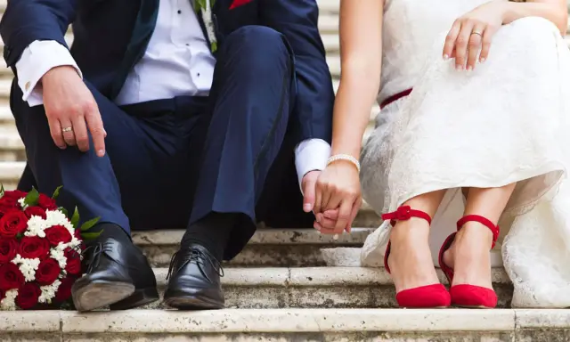 Brautpaar hält Händchen, rote Rosen und rote Schuhe. Die Frage "wie kurzfristig kann man heiraten" beschäftigt viele Paare.