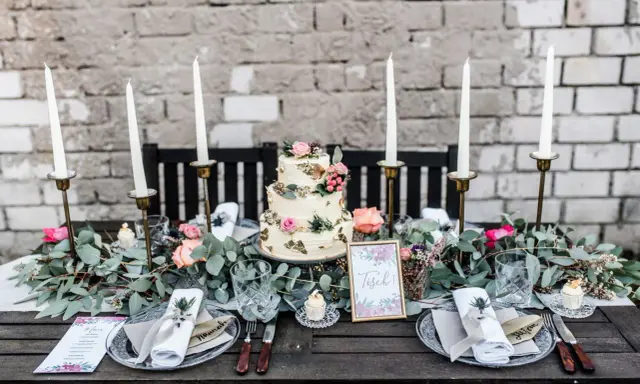 Festlich gedeckter Tisch für eine Hochzeit im Industrial Style mit dreistöckiger Torte, Kerzen und floraler Deko.