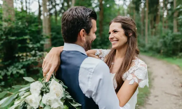 Ein glückliches Brautpaar umarmt sich im Wald. Sie wollten heimlich heiraten und genießen diesen intimen Moment.