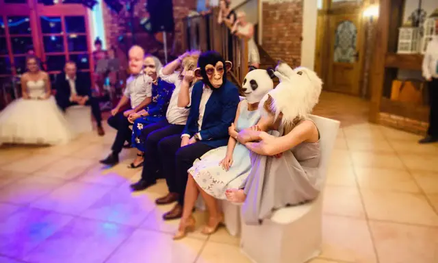 Gäste in Tiermasken warten auf kurzweilige Hochzeitsspiele. Ein Affe, ein Panda und ein weißes Tier sind zu sehen.