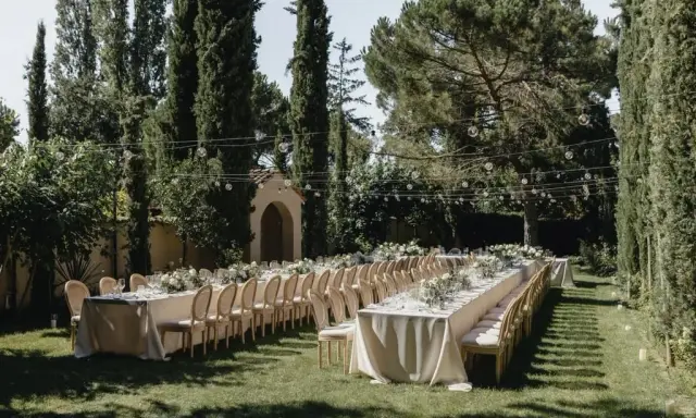 Festlich gedeckte lange Tafel im Garten, umgeben von Zypressen und Bäumen. Perfekt für Hochzeitslocation-Fragen.