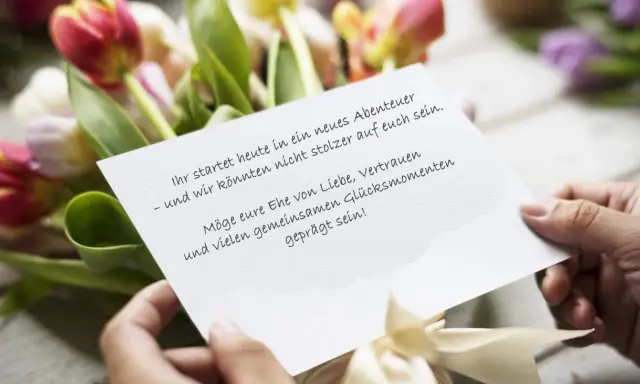 Hände halten eine Karte mit emotionalen Hochzeitswünschen vor einem Tulpenstrauß.