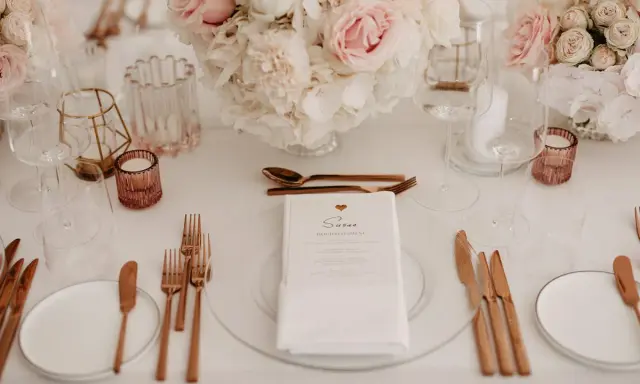 Ein festlich gedeckter Tisch mit Blumen, Gläsern und roségoldenem Besteck. Ein Hochzeitsmenü für Susan, perfekt arrangiert vom wedding planer.