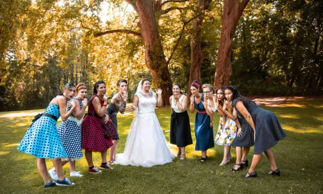 Brautjungfern in Polka-Dot-Kleidern und die Braut in Weiß posieren für eine fröhliche Rockabilly-Hochzeit im Freien.