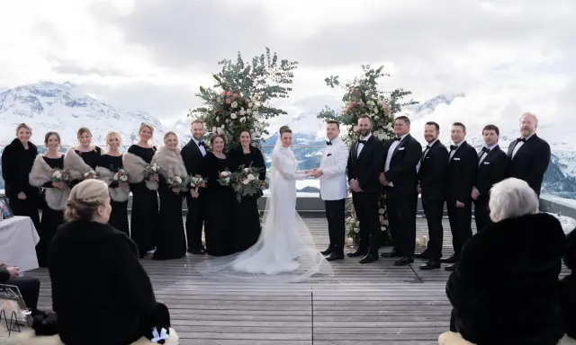 Brautpaar und Hochzeitsgesellschaft vor schneebedeckten Bergen. Eine wunderschöne Hochzeit in den Bergen mit Brautjungfern in schwarzen Kleidern und Männern in Anzügen.