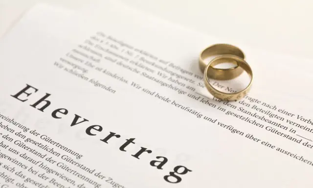 Zwei goldene Eheringe liegen auf einem Dokument mit der Überschrift "Ehevertrag". Eine Ehevertrag Vorlage, die die rechtlichen Vereinbarungen für die Ehe festhält.