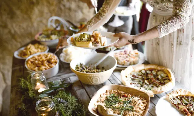 Festliches Buffet mit vielen Köstlichkeiten, perfekt für eine vegane Hochzeit. Teller werden mit leckerem Essen gefüllt.