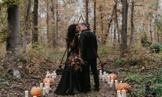 Ein Brautpaar küsst sich im Wald bei Kerzenlicht und Kürbissen. Eine romantische Halloween-Hochzeit im Herbst.