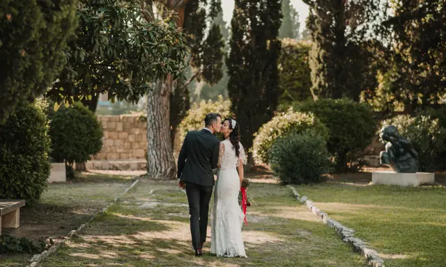 Ein Brautpaar küsst sich im Park. Die Braut trägt ein Spitzenkleid, der Bräutigam einen dunklen Anzug. Eine kroatische Hochzeit im Grünen.