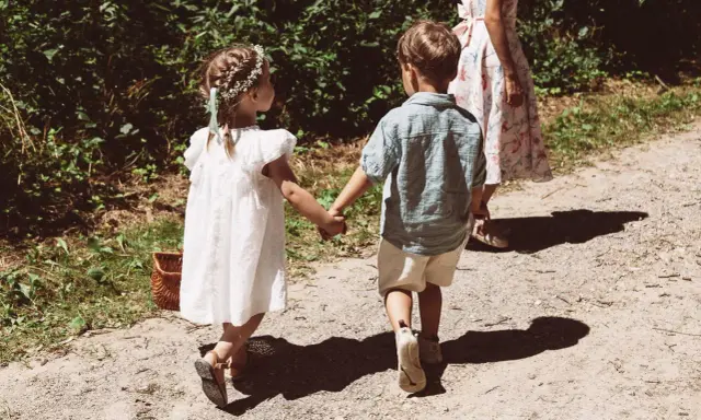 Zwei Kinder, ein Mädchen mit Blumenkranz und ein Junge, halten Händchen auf dem Weg zu einer Hochzeit mit Kindern.