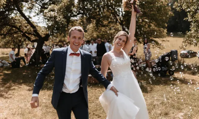 Glückliches Brautpaar im Freien, umgeben von Seifenblasen. Sie strahlen und scheinen gerade ihren Hochzeitstanz gelernt zu haben und feiern diesen besonderen Moment.