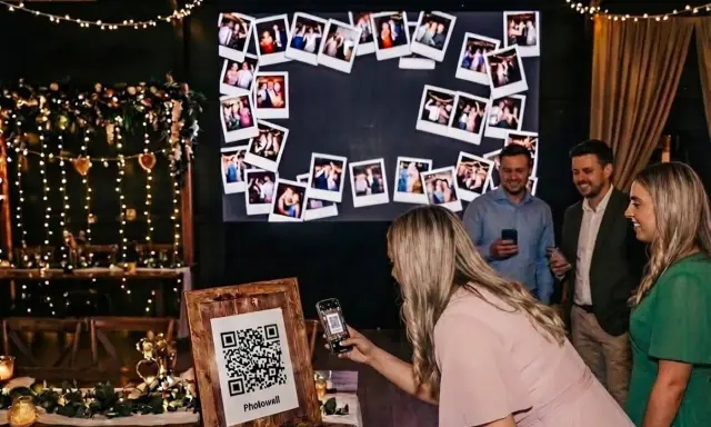 Eine Frau scannt mit ihrem Handy einen QR-Code für eine Photowall. Eine tolle Idee für ein Hochzeitsprogramm mit vielen Erinnerungsfotos.