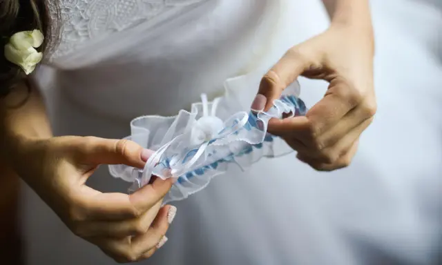 Braut hält ein weißes Strumpfband mit blauen Akzenten. Das Strumpfband ist ein traditionelles Symbol für Glück bei der Hochzeit.