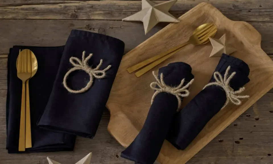 Serviettenringe selber machen: Dunkle Stoffservietten mit rustikalen Geweih-Motiven aus Jute, dazu goldene Besteckteile und Papiersterne.