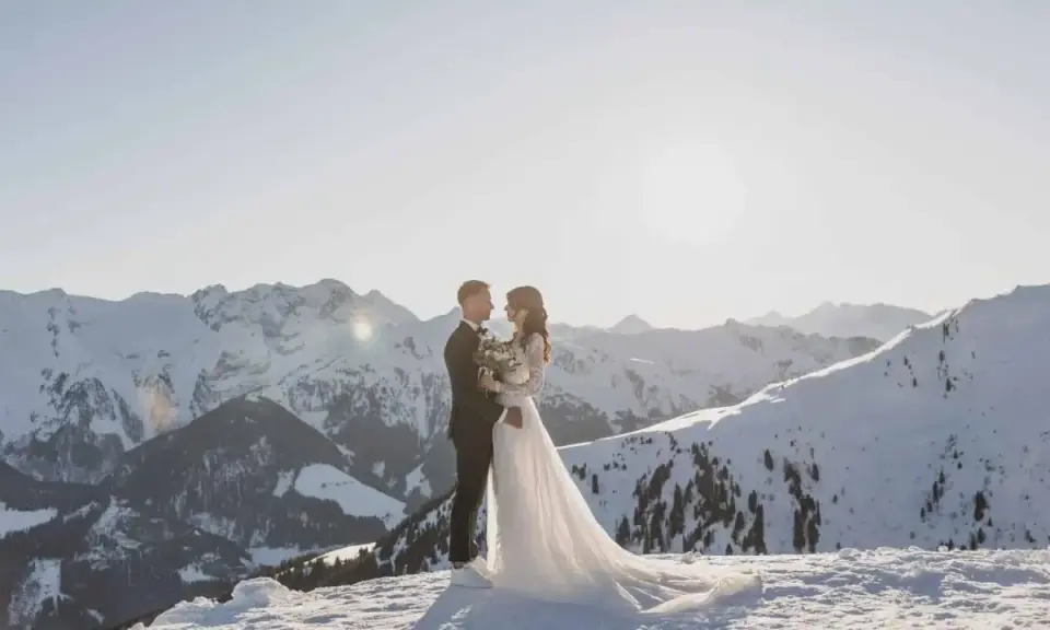 Ein Brautpaar steht sich in der verschneiten Berglandschaft gegenüber. Ihre **Hochzeit im Schnee** ist ein magischer Moment vor der Kulisse schneebedeckter Gipfel.